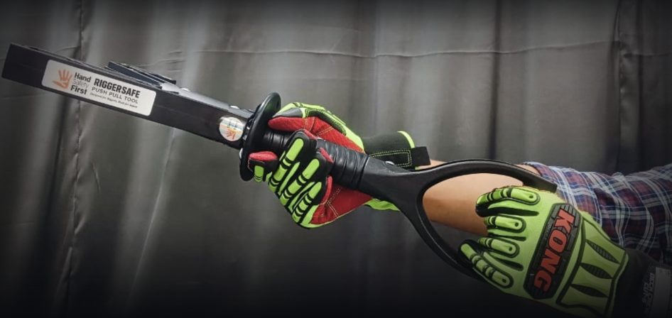 Operator's gloved hand gripping the RiggerSafe® D-handle, tool extended toward the work